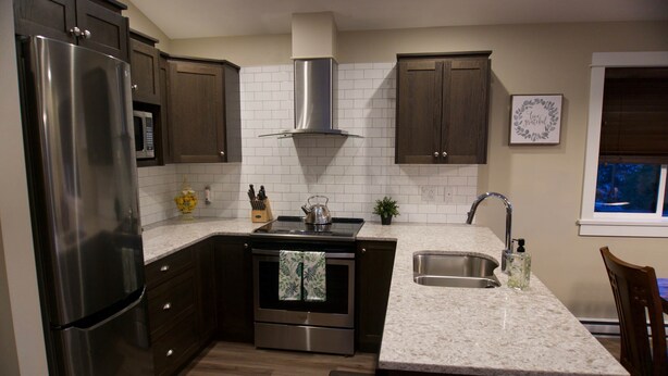 A modern kitchen with dark wood cabinets, stainless steel appliances, a white tiled backsplash, and a granite countertop. - Shore 2 Please (Oceanview with Amazing Views) (Port Renfrew)