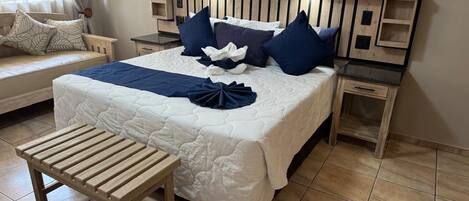 Una cama bien tendida con cabecera de madera, una mesita de noche y un banco.