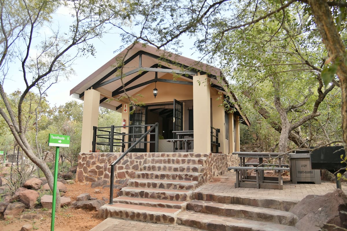A stone staircase leading to a covered pavilion with a bench and trash bin nearby.