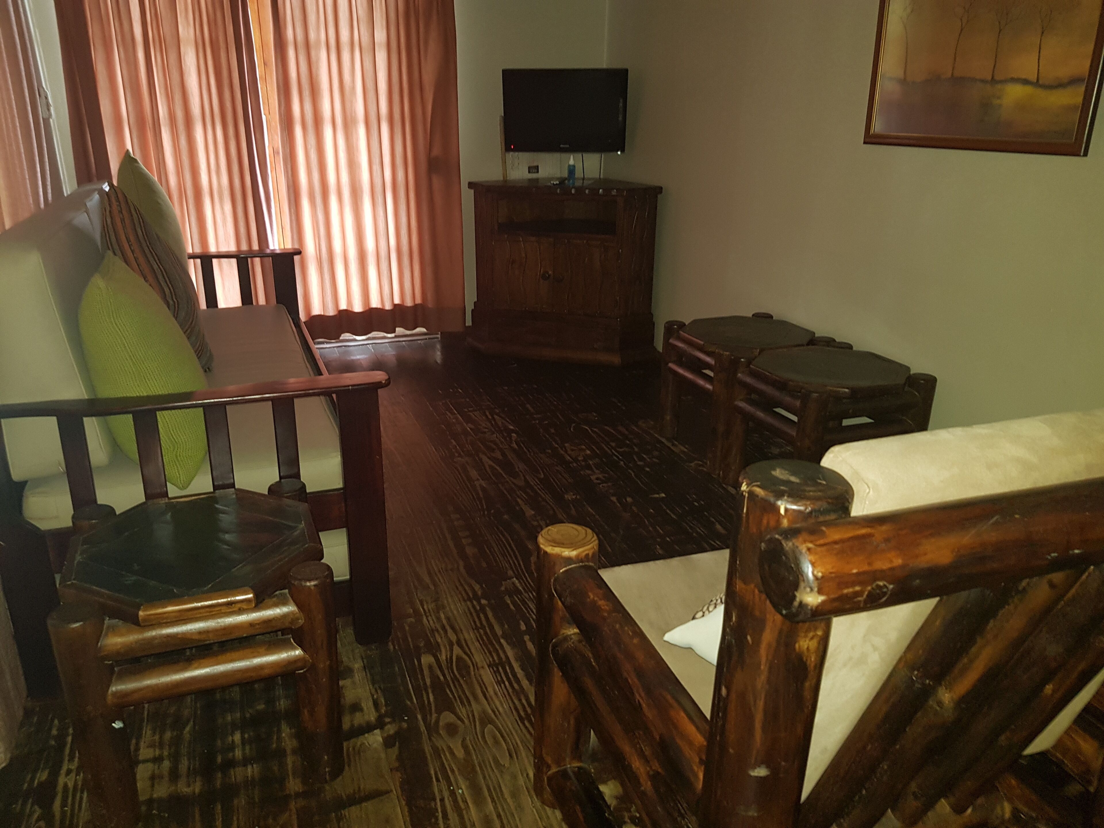A wooden-floored living room with a sofa, armchairs, and a small table. A television is mounted on the wall above a wooden cabinet.