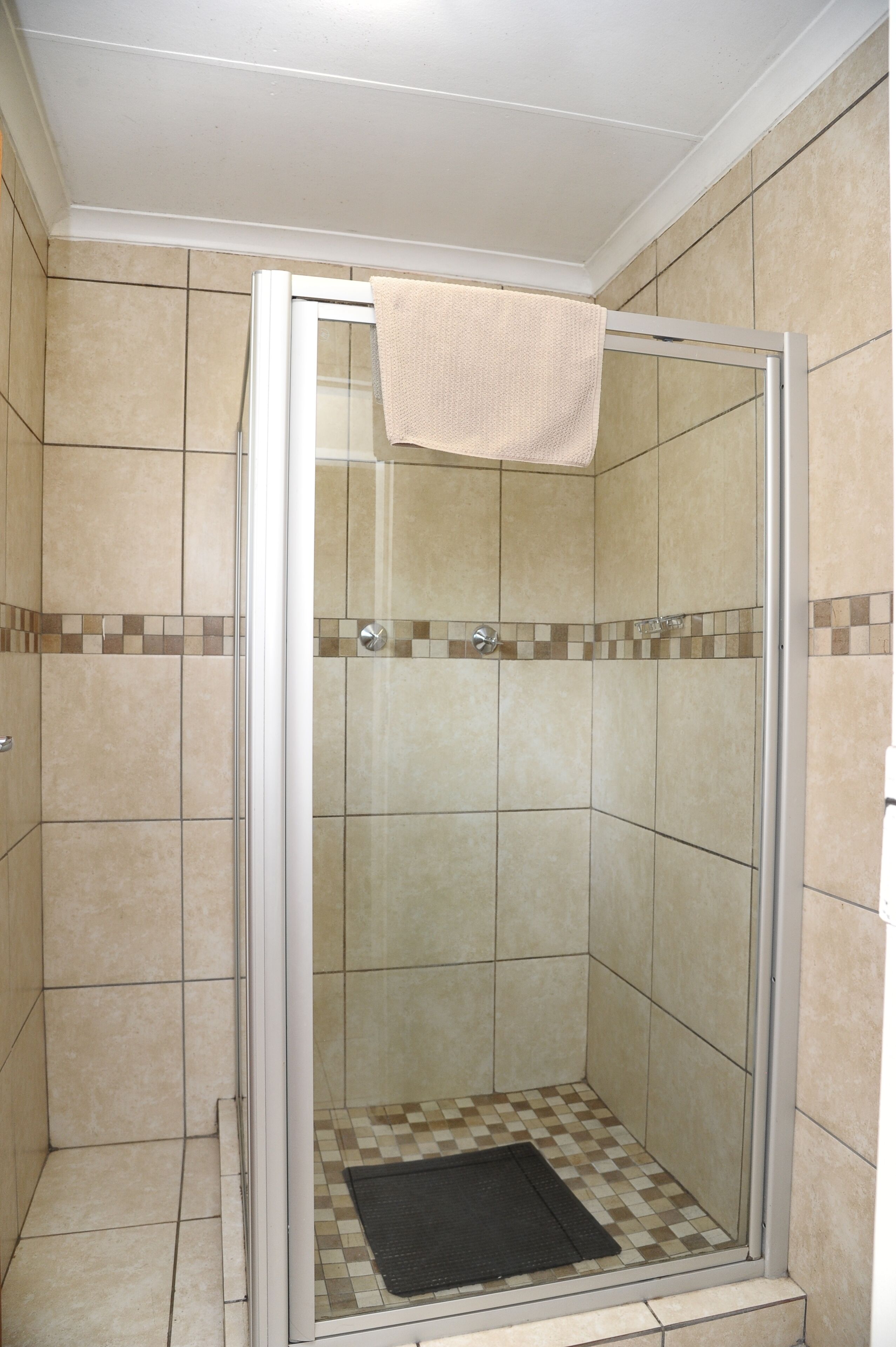 A glass-enclosed shower with beige tiles and a checkered pattern at the bottom.