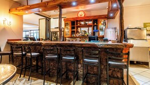 Uma área de bar com bancada de pedra, vários bancos e estrutura de teto em madeira.