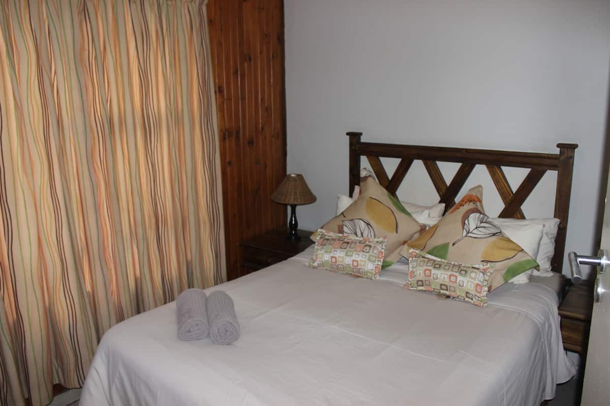 A neatly made bed with two rolled towels, a wooden headboard, and a patterned pillow.