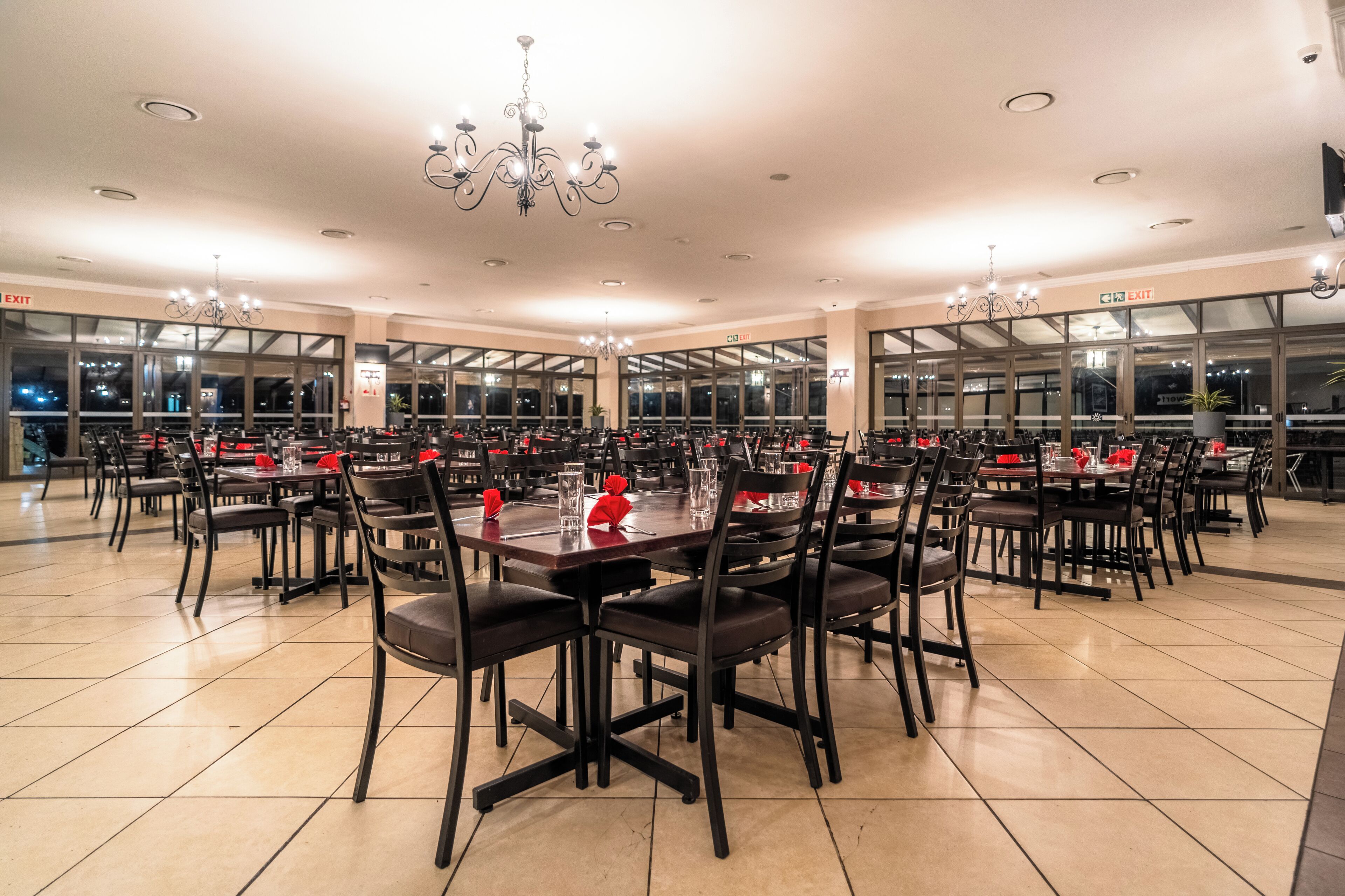 Un amplio comedor con varias mesas y sillas, ventanas grandes y señalización de salida.