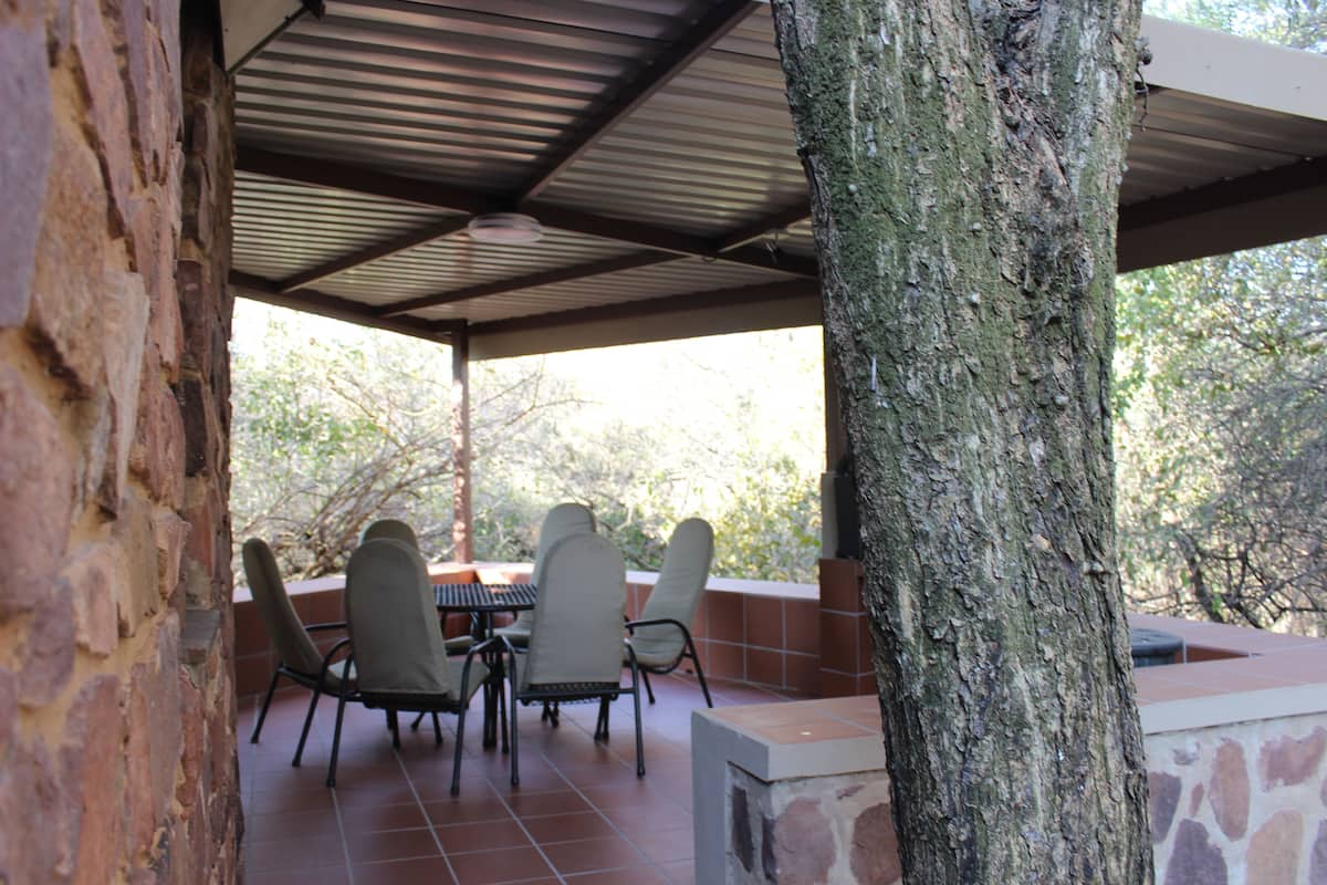 An outdoor patio with a stone table and four chairs, surrounded by a stone wall and a tree.