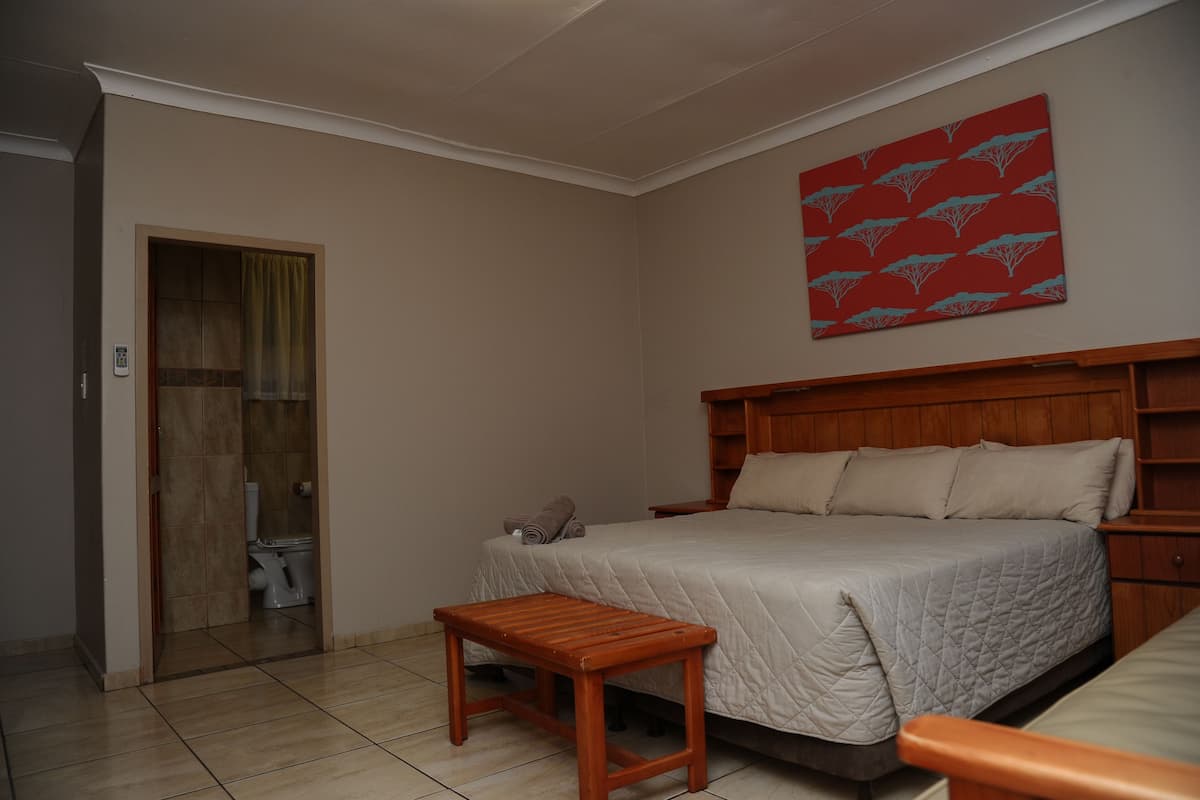 A bedroom with a bed, a wooden headboard, a bedside table, and a red patterned wall hanging.