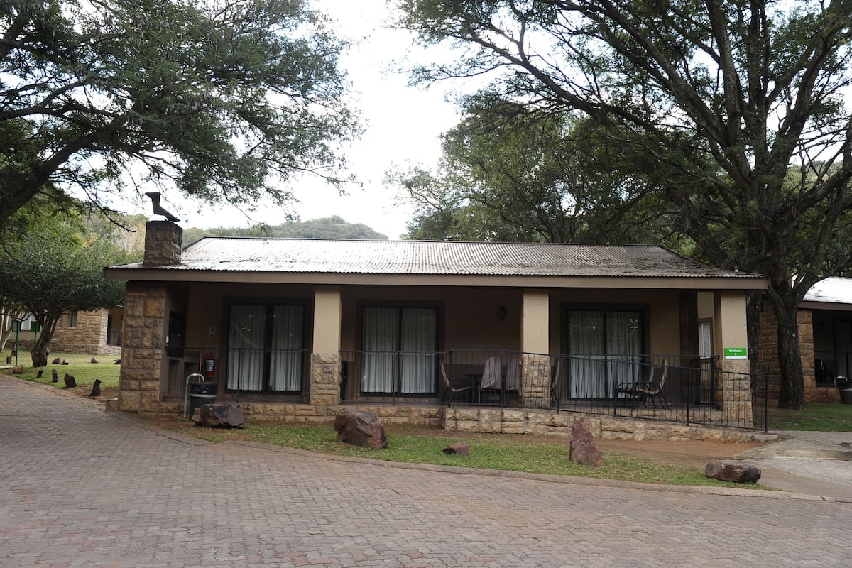 A building with a stone facade, a metal roof, and a porch with chairs.