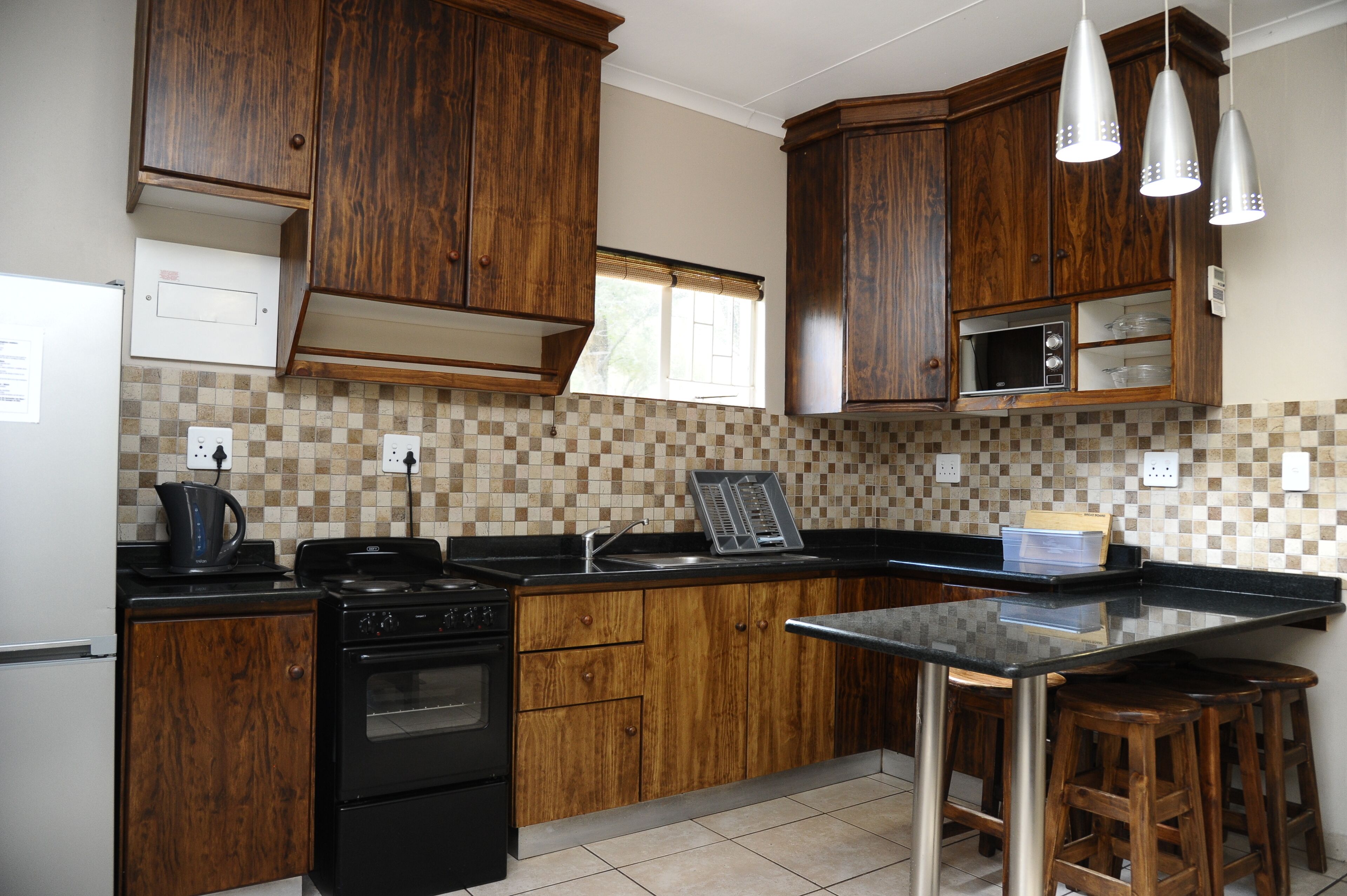 Una cocina con armarios de madera, encimera negra, estufa y ventana con persianas.