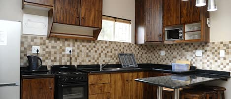 Una cocina con armarios de madera, encimera negra, estufa y ventana con persianas.