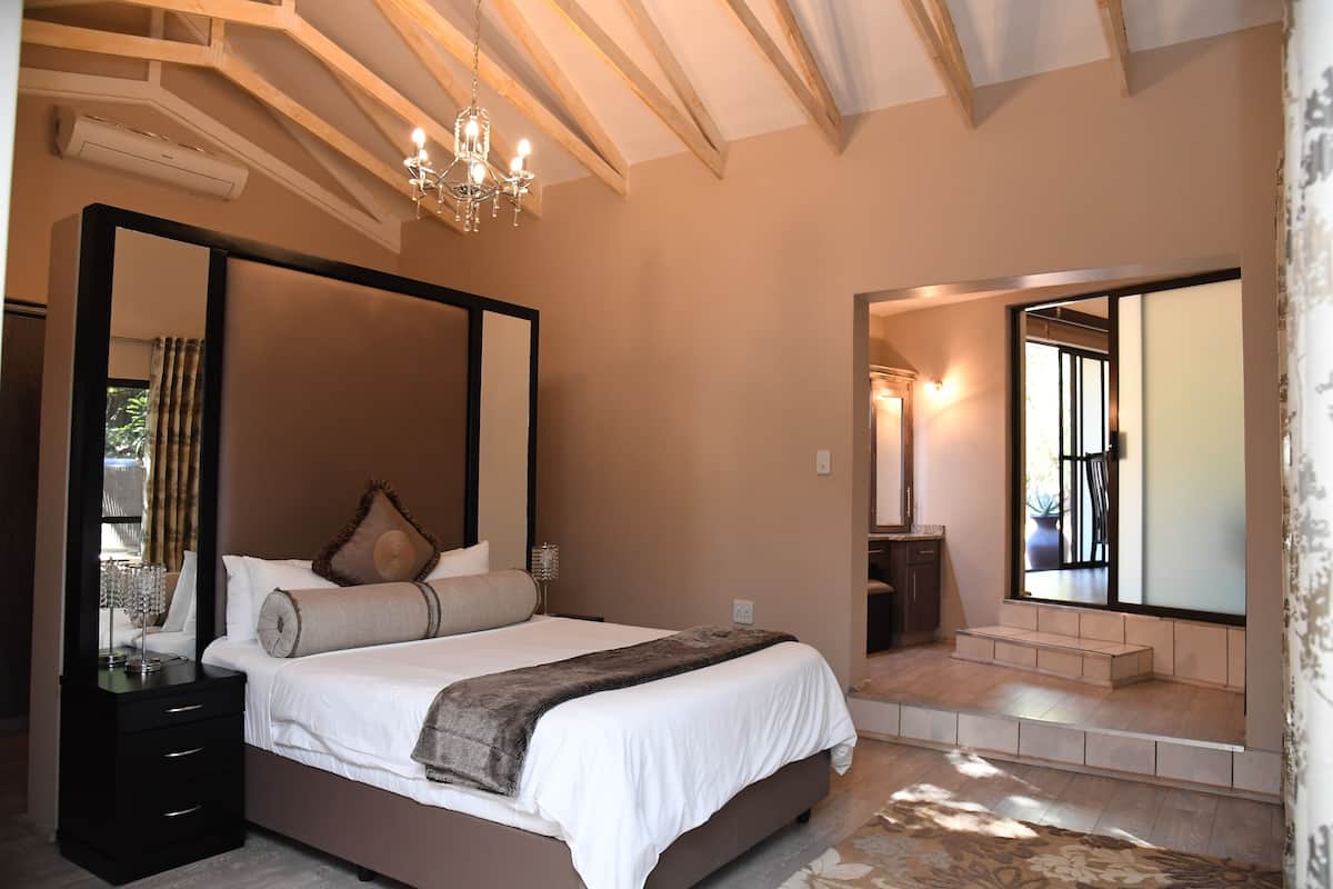 A bedroom with a large bed, a mirror, a chandelier, and a view of the outside.