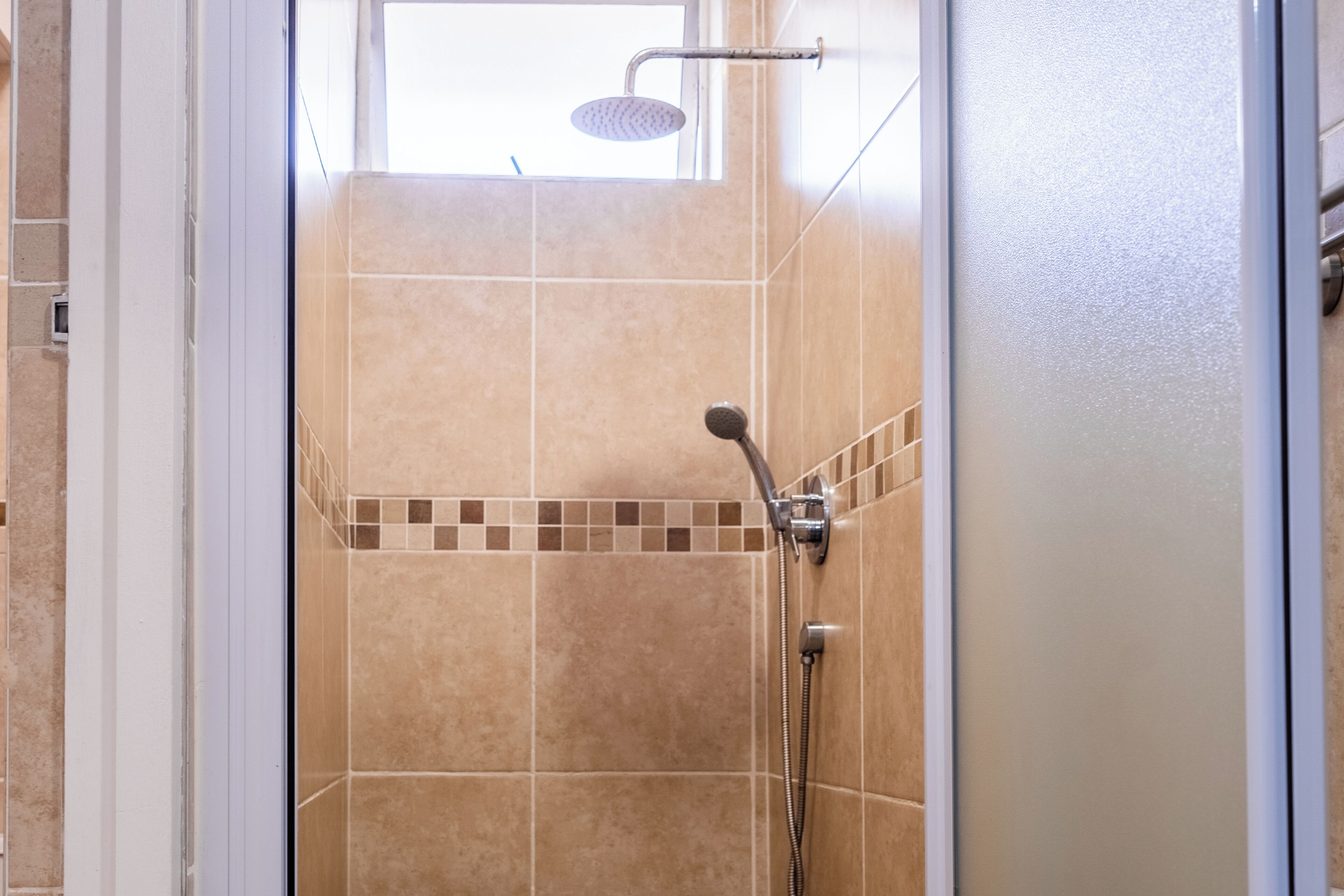 A shower area with a glass door, tiled walls, and a handheld showerhead.