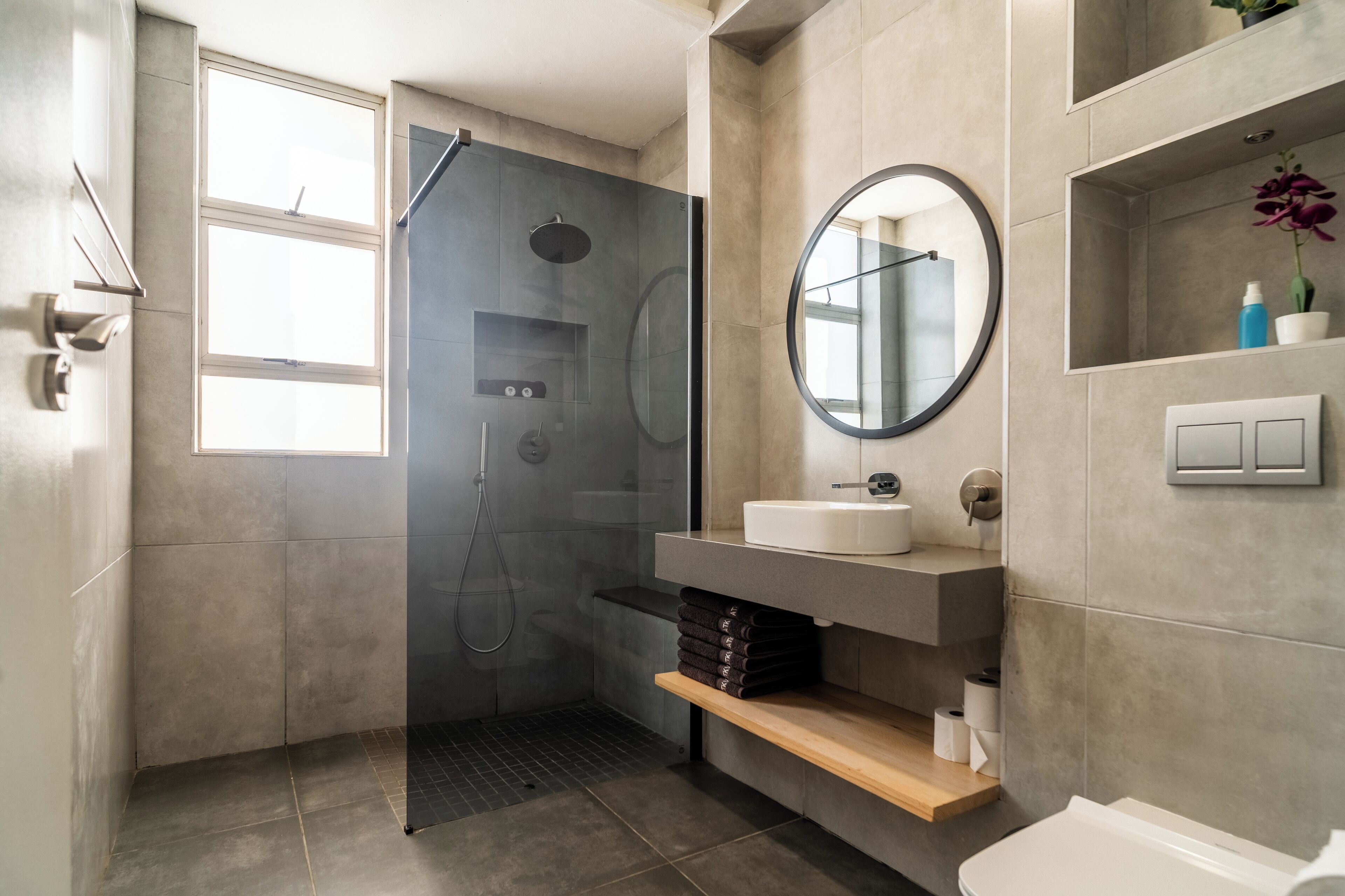 A modern bathroom with a glass-enclosed shower, a round mirror, a sink, and a toilet.