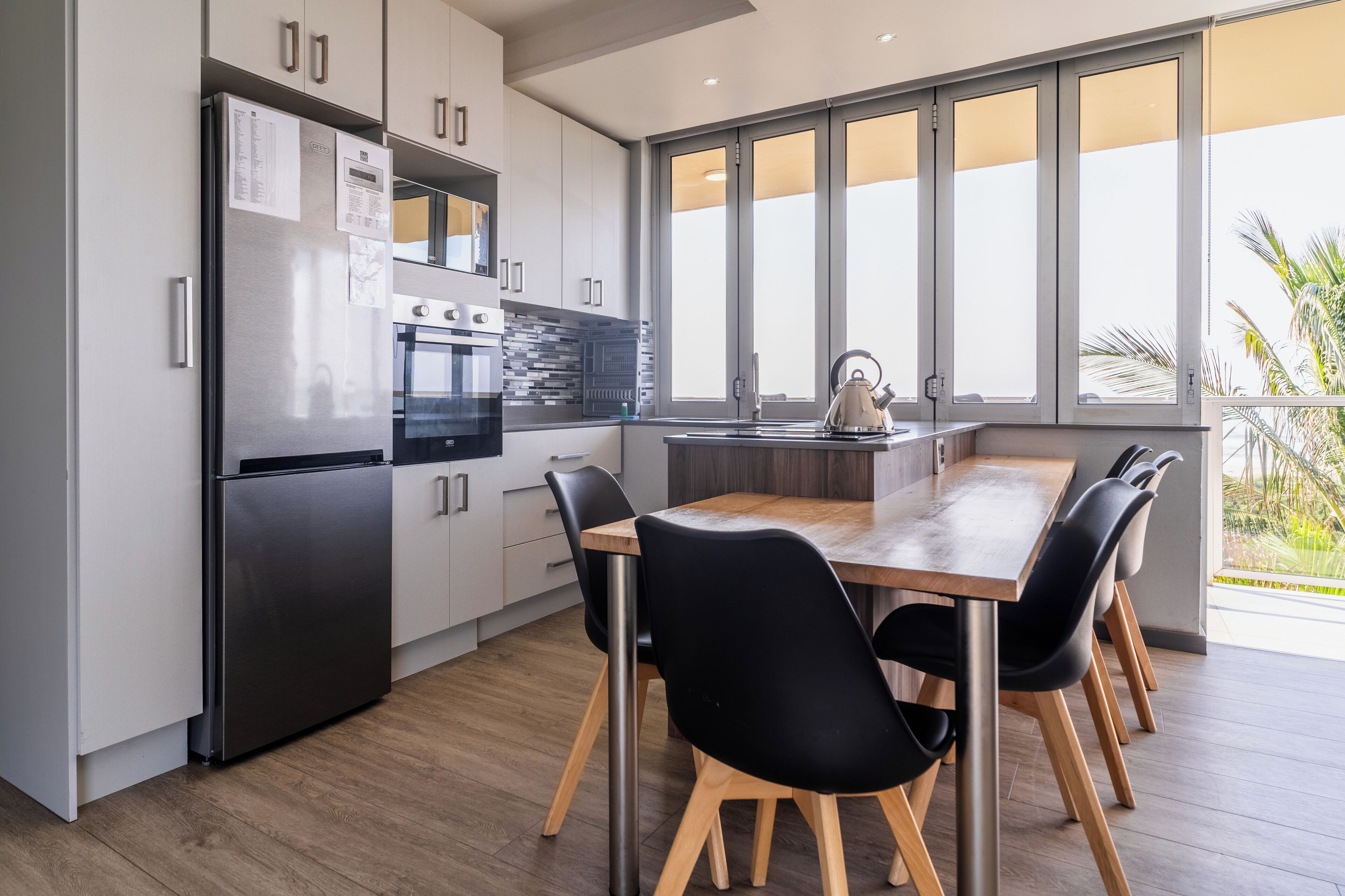A modern kitchen with stainless steel appliances, a wooden dining table, and black chairs.