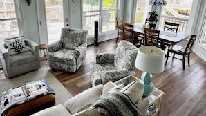 A spacious living room with a dining area, large windows, and a ceiling fan. - BEAUTIFUL OCEANFRONT with gorgeous views! 2 king beds, 3 queen beds and 4 twins. (Emerald Isle)