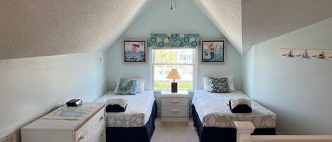 A bedroom with two single beds, a ceiling fan, a desk, and a window with a view of the outside.