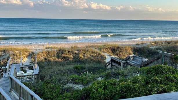 A beach view with a wooden deck, a small building, and a sandy beach. - BEAUTIFUL OCEANFRONT with gorgeous views! 2 king beds, 3 queen beds and 4 twins. (Emerald Isle)