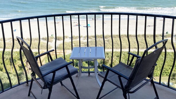 A balcony with two chairs and a table, overlooking a beach with waves. - Lifes a beach on Myrtle Beach (Myrtle Beach)