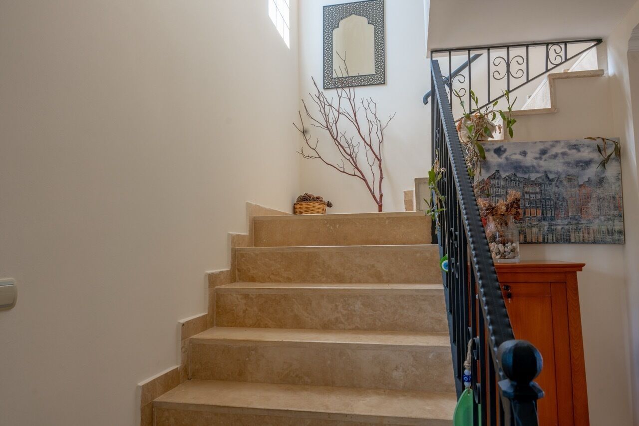 Una escala amb graons beix, un quadre penjat a la paret, una branca decorativa i una pintura d'un paisatge urbà.