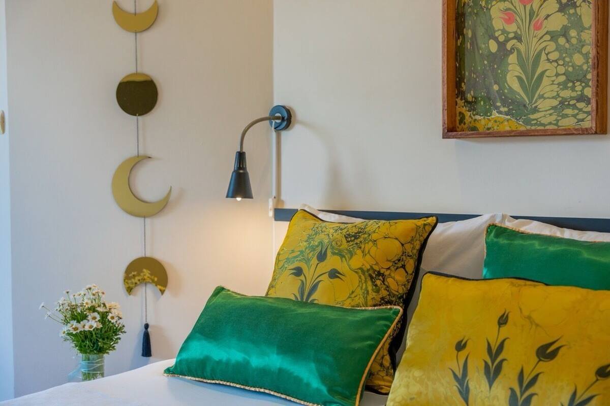A bed with green and yellow pillows, a wall-mounted lamp, and a wall decoration of circular shapes.