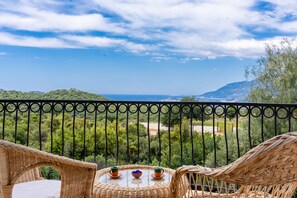 A balcony with wicker furniture and a table, overlooking a scenic landscape with hills and a view of the sea. - Lacitrus Villa Hotel (Kas)