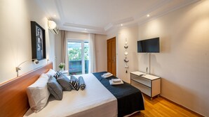 Hotellihuone, jossa on sänky, työpöytä, televisio ja parveke, jolta on näkymä.