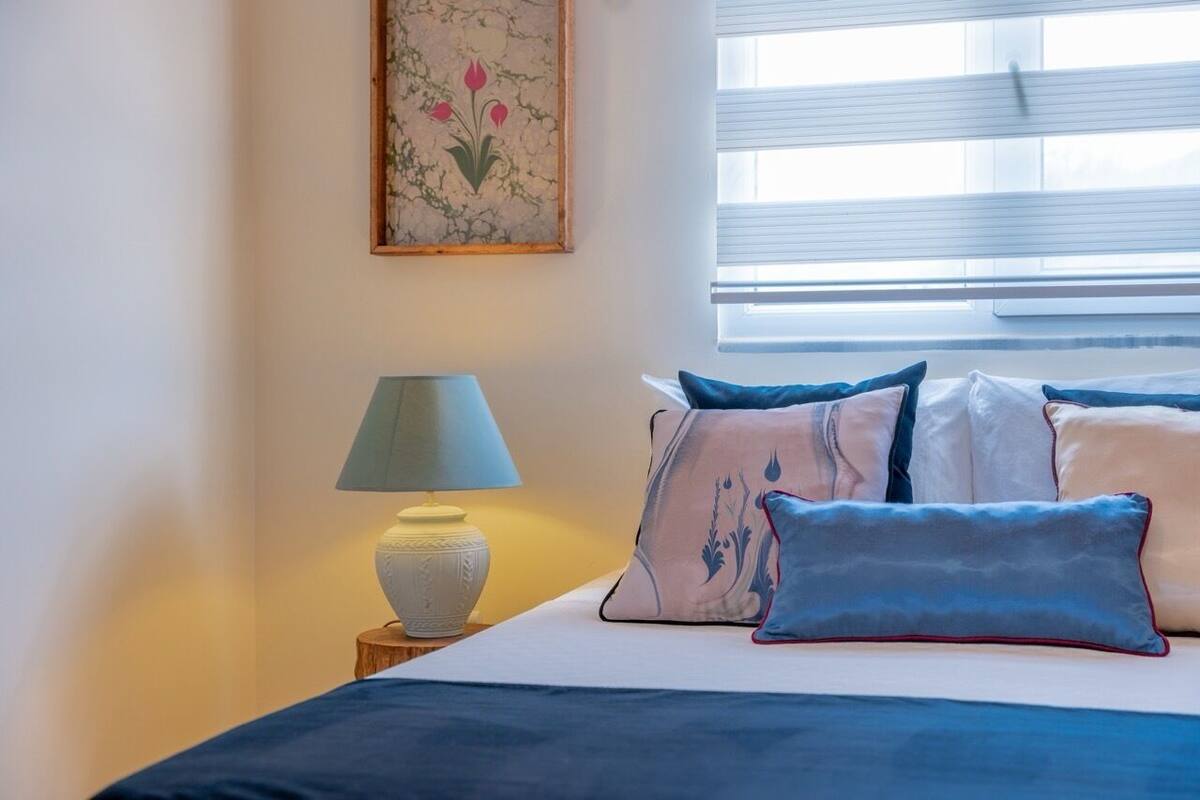 A bedroom with a bed, pillows, a bedside lamp, and a window with blinds.