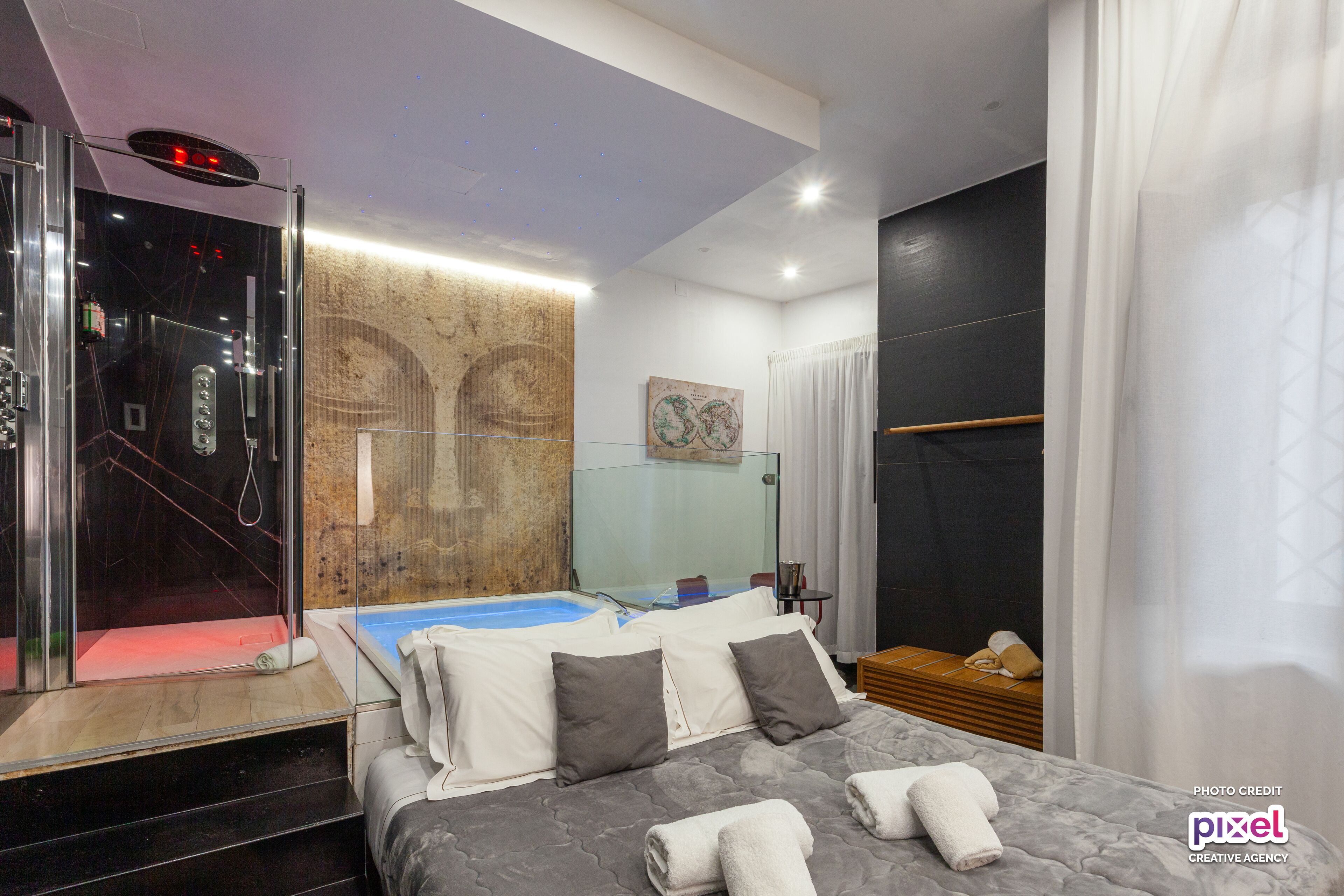Una camera d'albergo moderna con box doccia in vetro, un letto con biancheria grigia, un comodino in legno e una grande mappa appesa al muro.