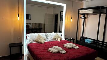 Una camera d'albergo moderna con un letto grande, un armadio a muro, un angolo salotto con un tavolino e un angolo cottura.