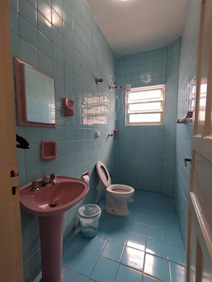 A bathroom with blue tiles, a pink sink, a toilet, a window, and a mirror. - Pousada Recanto da Praia (Bertioga)