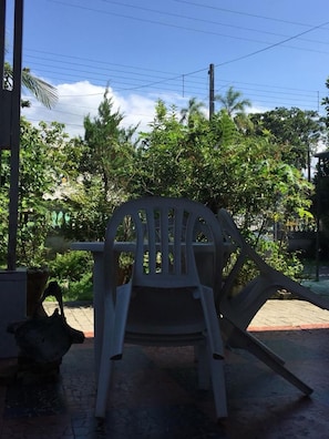 A plastic chair outdoors with a brick floor and greenery in the background. - Pousada Recanto da Praia (Bertioga)