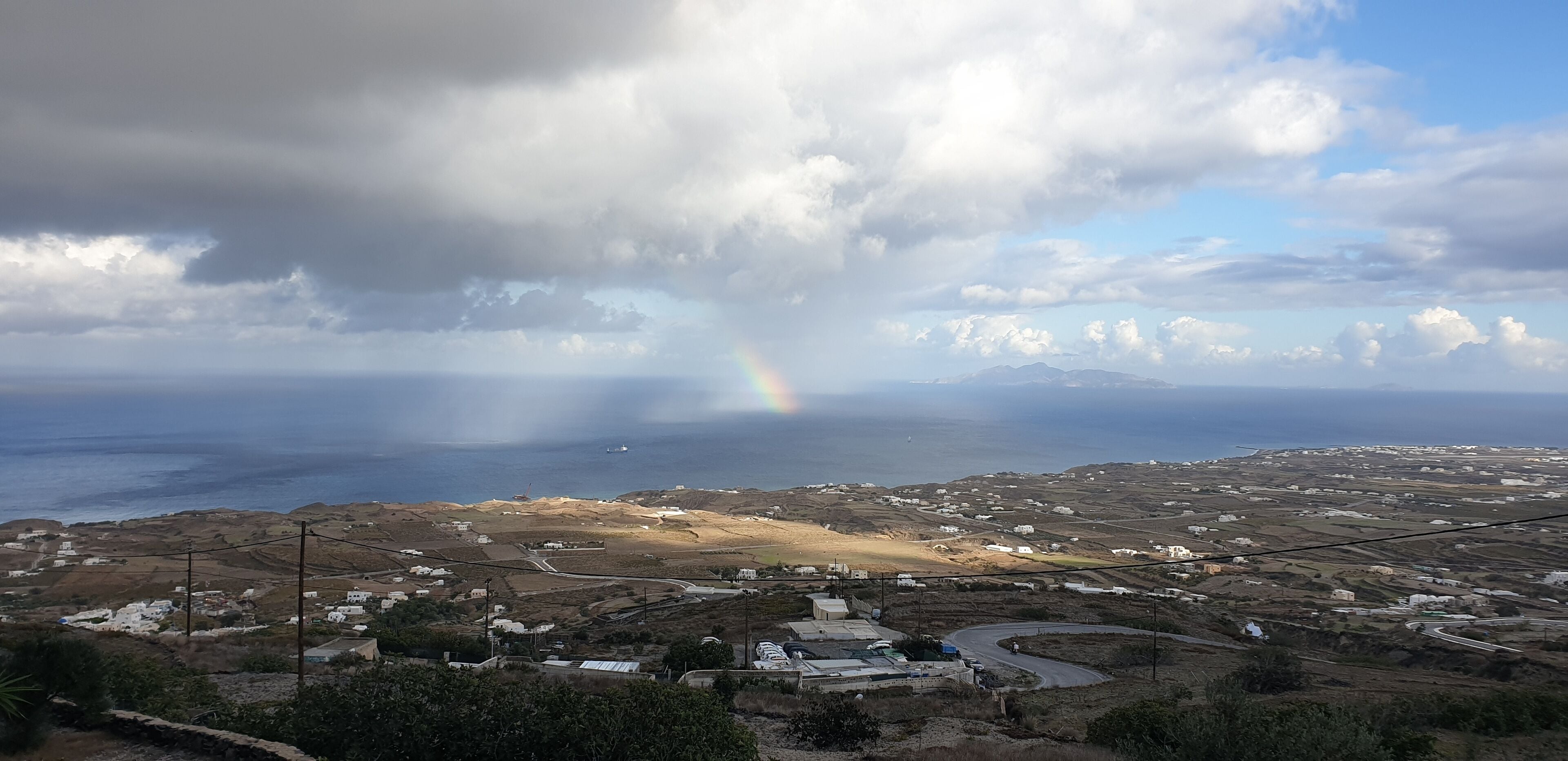A coastal landscape with a winding road, scattered buildings, and a distant view of the sea.