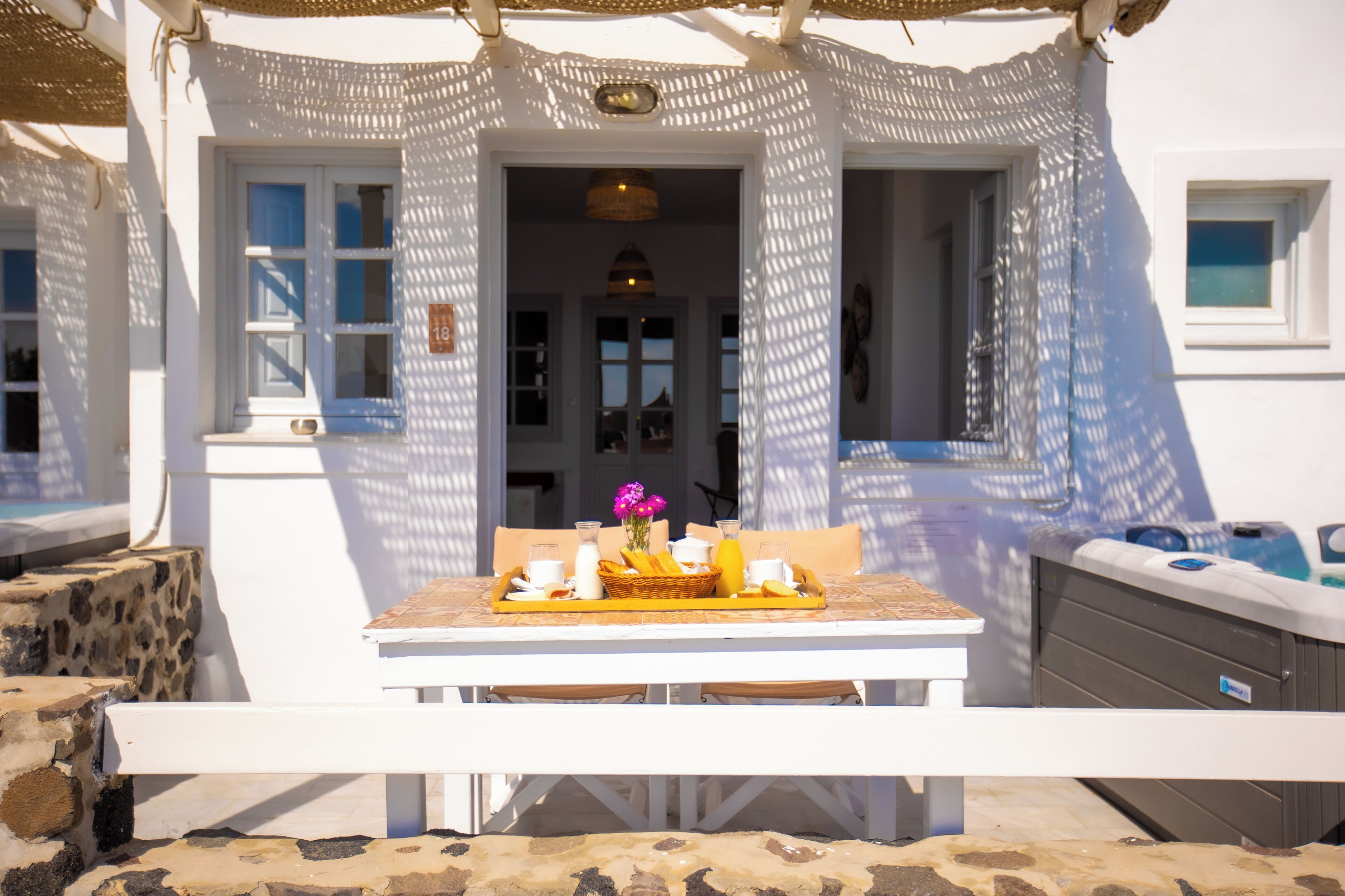 Un espacio exterior de comedor blanco con una mesa lista para el desayuno, incluyendo pan, huevos y bebidas.