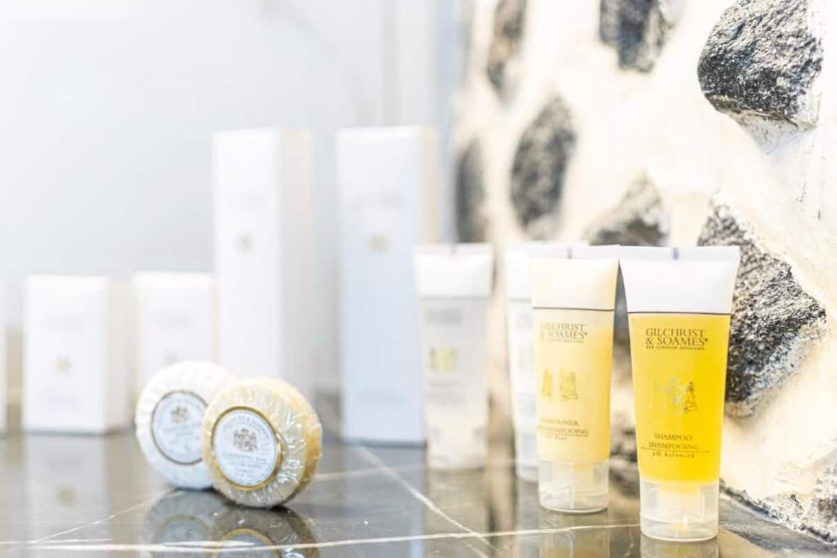 Mehrere Flaschen Gilchrist & Soames Shampoo und eine Seife auf einer spiegelnden Oberfläche, mit einer Steinwand im Hintergrund.