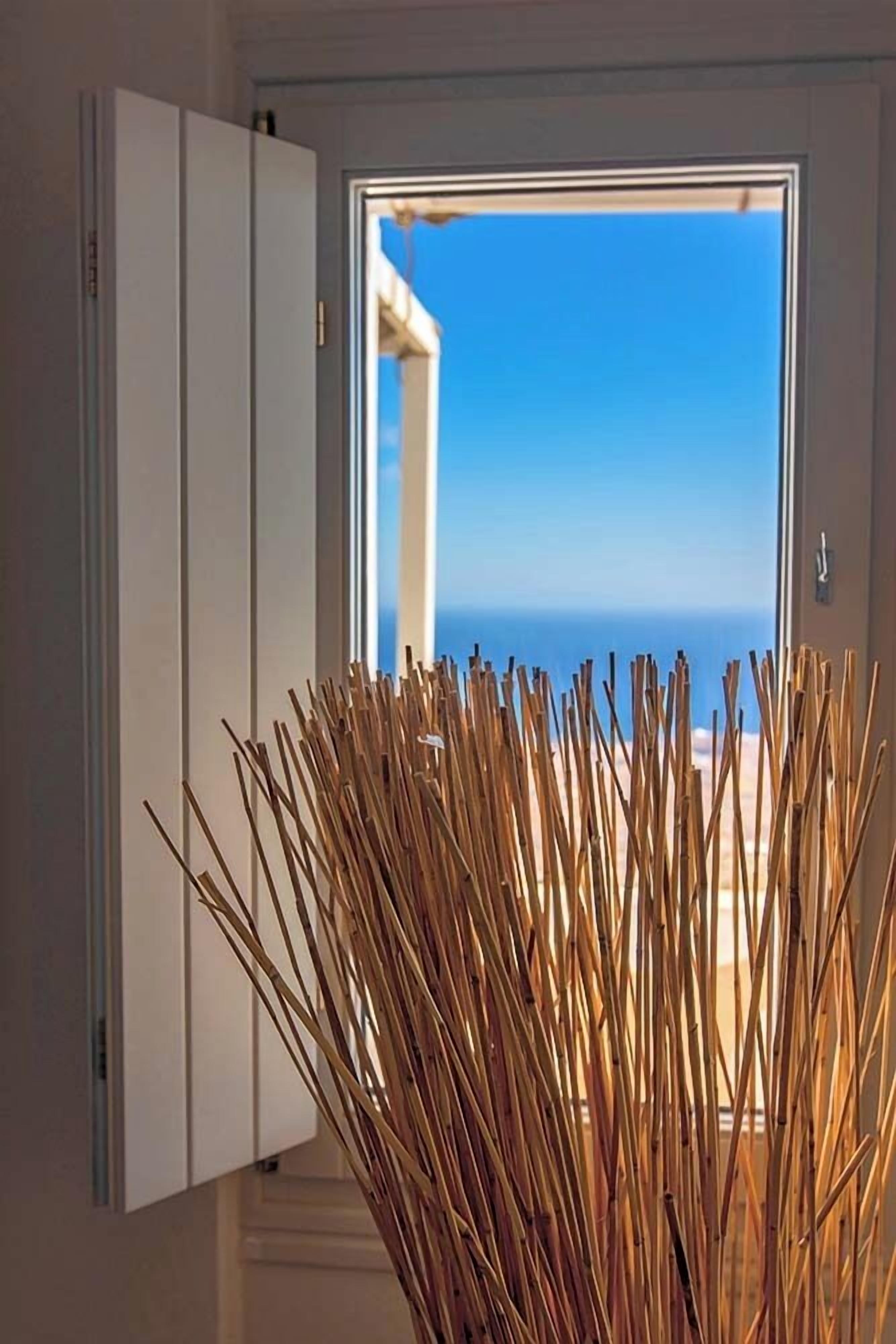 A room with a view of the sea through a window, a white cabinet, and a decorative arrangement of sticks.
