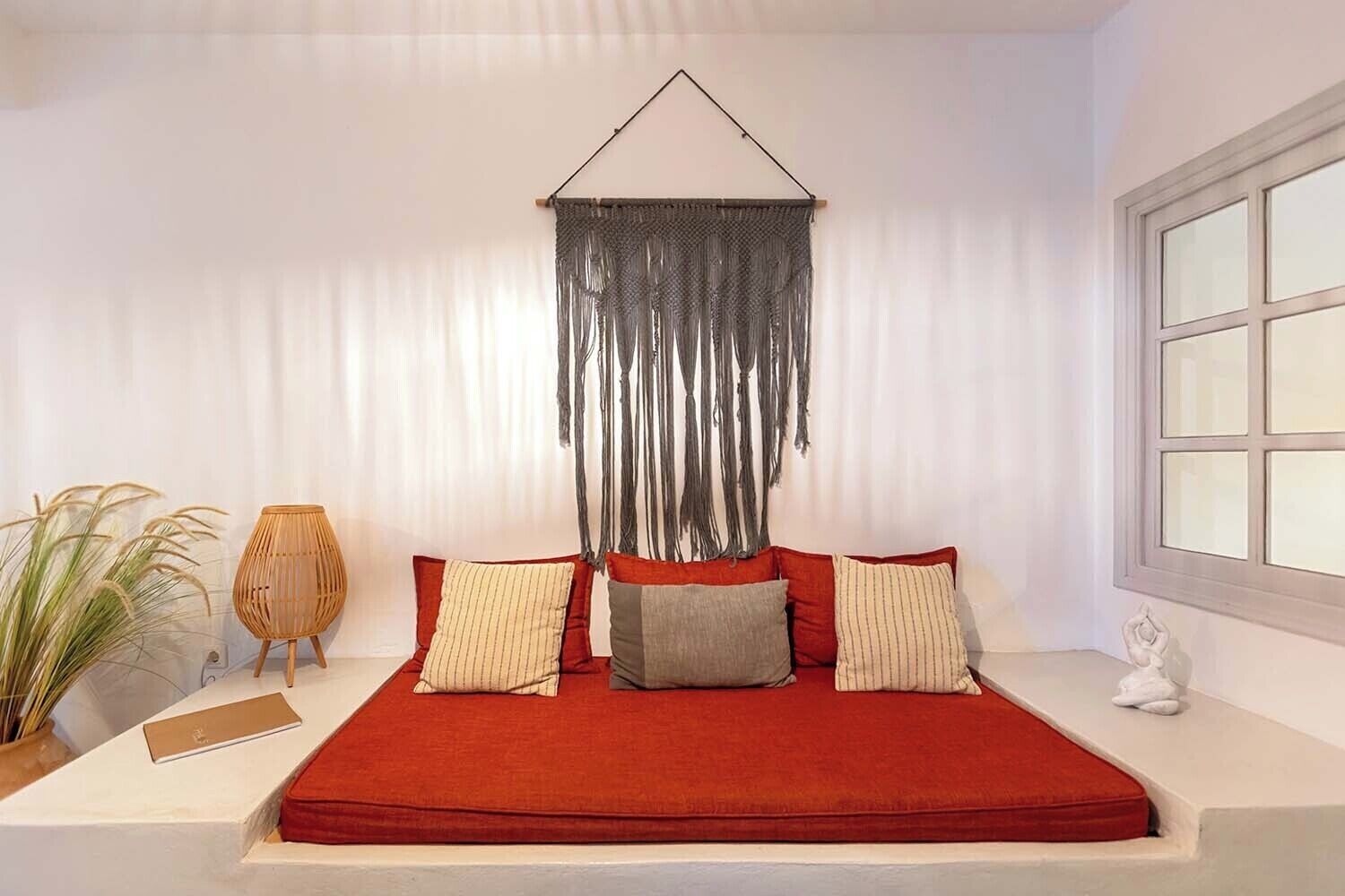 Una habitación con cama, ventana y un adorno de macramé en la pared.