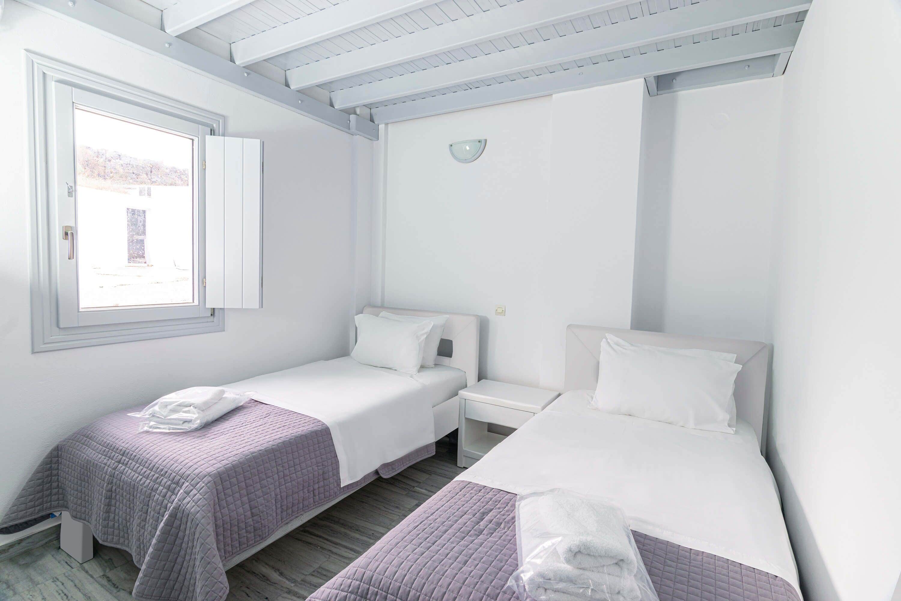 Una habitación con dos camas individuales, una mesita de noche pequeña, una ventana y una lámpara en el techo.