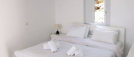 A clean, white hotel room with a bed, a bedside lamp, and an air conditioning unit.