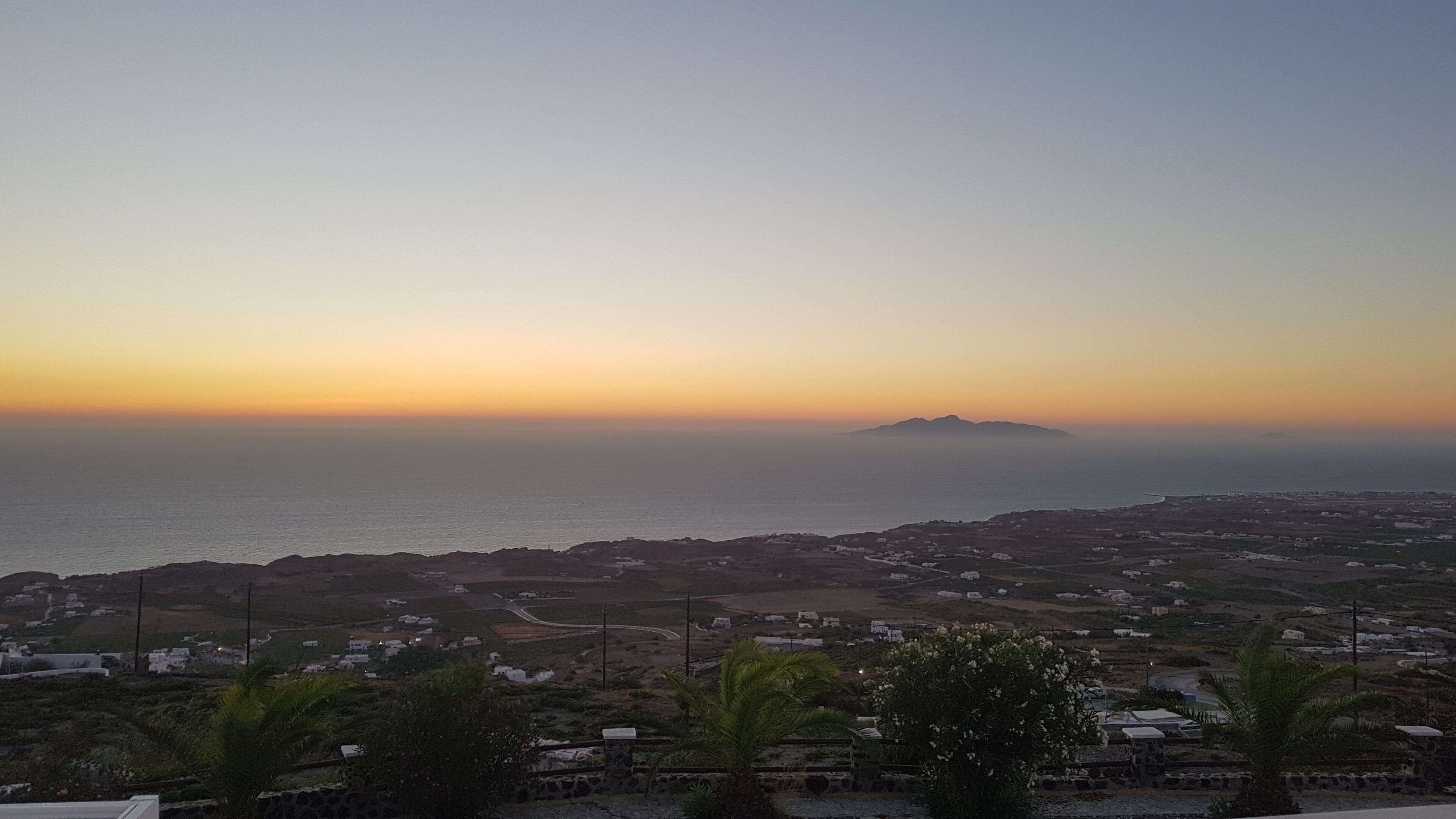 Paisaje costero con vista al mar y montañas distantes al atardecer.