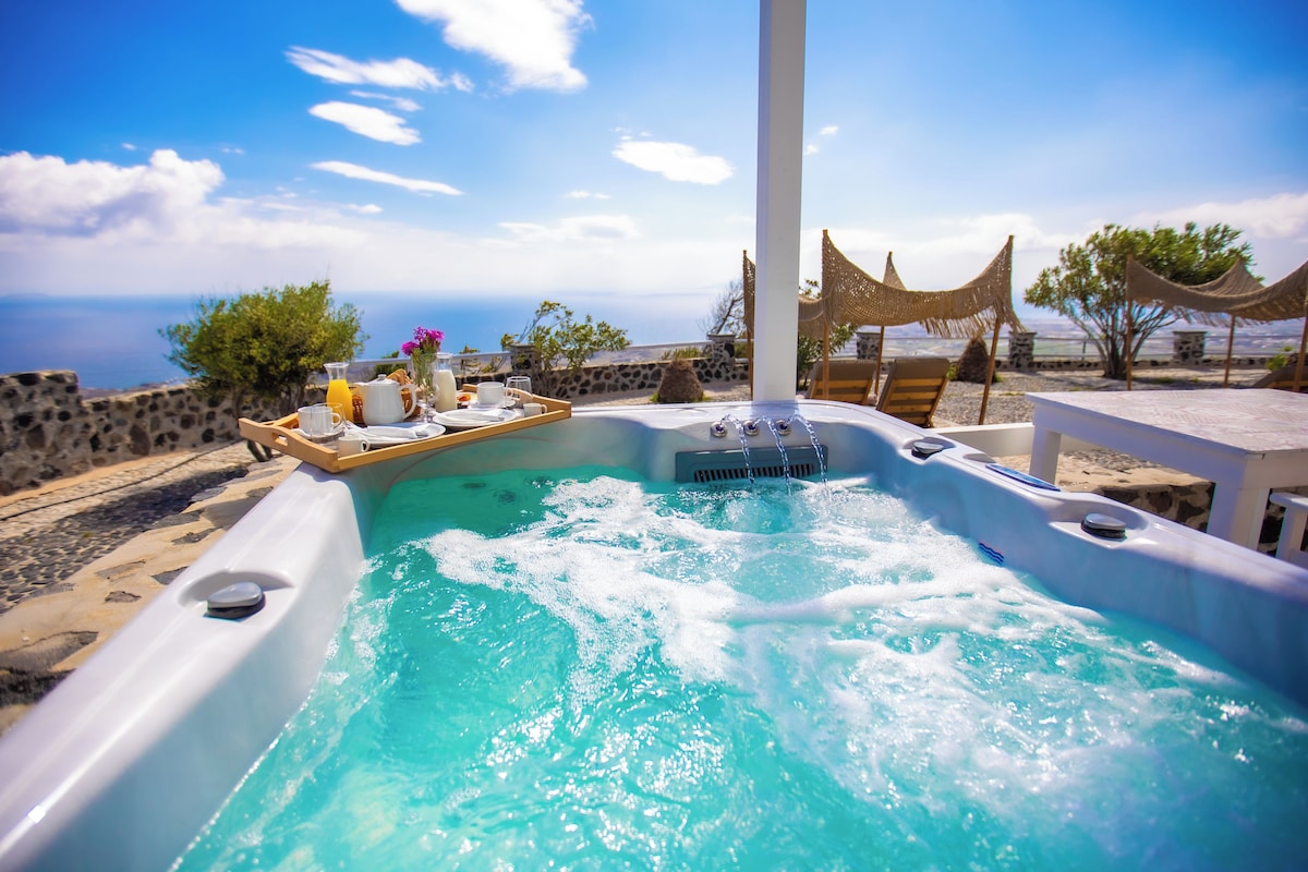 A hot tub with a wooden tray and drinks, surrounded by stone walls and a view of the sea.