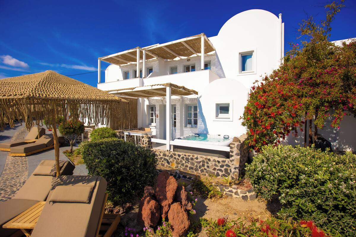 A white building with a pool, lounge chairs, and a thatched umbrella.