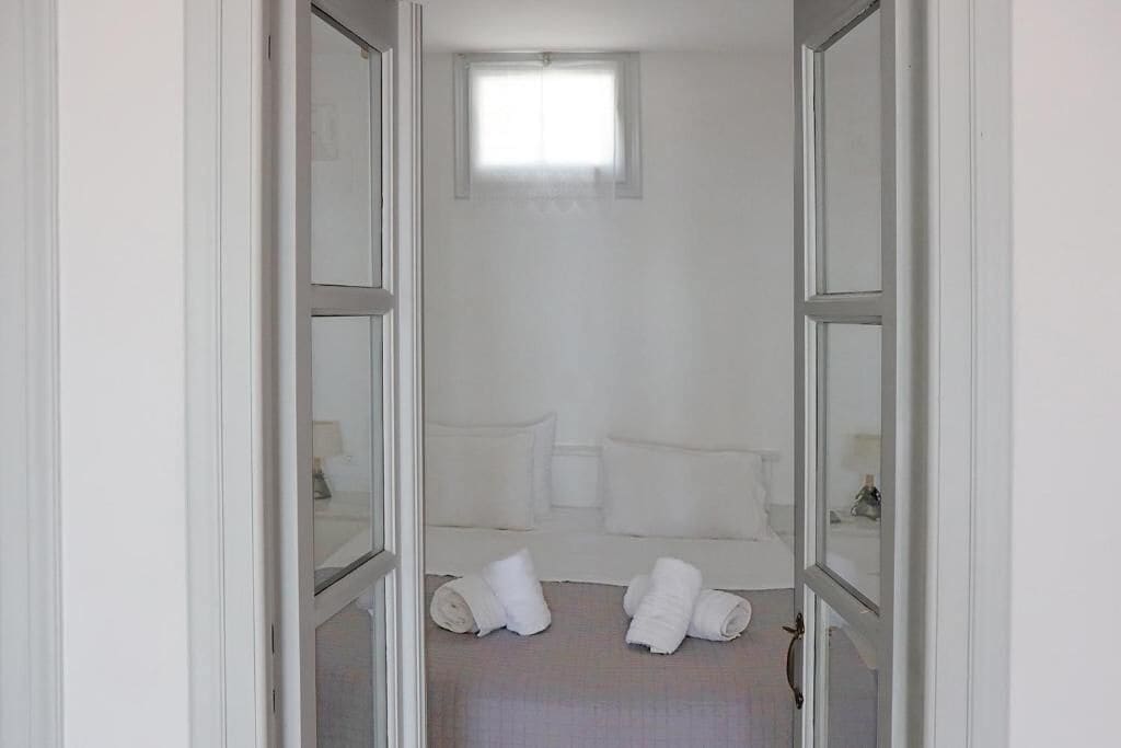A narrow hallway leading to a bedroom with a bed, pillows, and rolled towels on the floor.