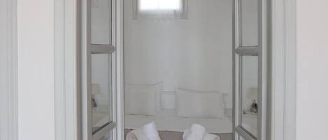 A narrow hallway leading to a bedroom with a bed, pillows, and rolled towels on the floor.