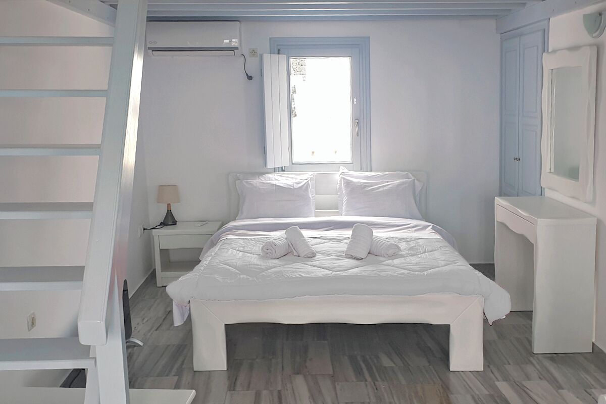 Une chambre à coucher avec un lit, une table de chevet, une lampe, une fenêtre et un miroir.
