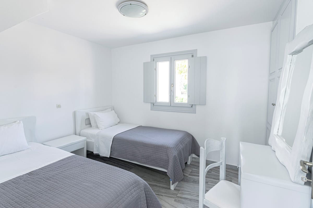Ein Zimmer mit zwei Betten, einem Fenster, einem weißen Kleiderschrank und einem weißen Stuhl.