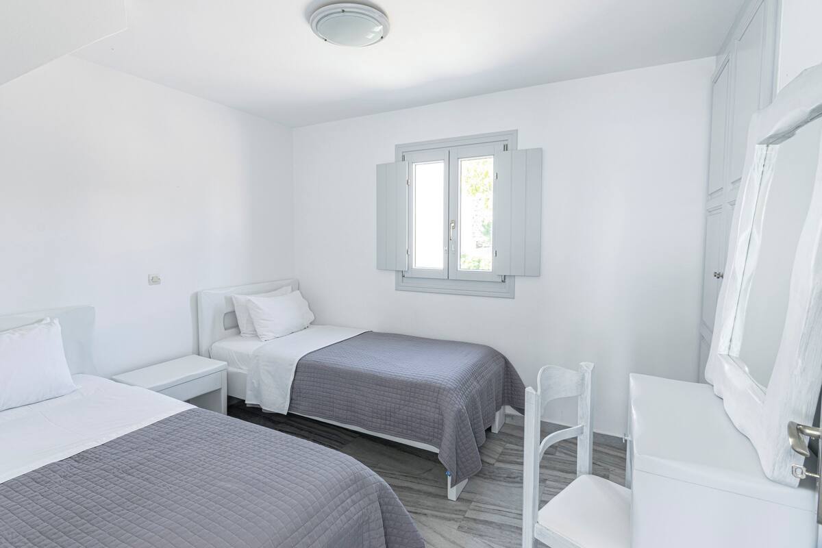 A room with two beds, a window, a white wardrobe, and a white chair.