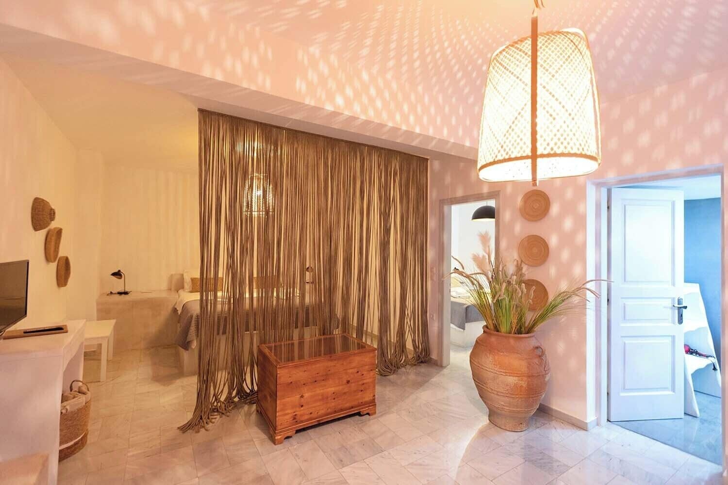 A modern living room with a sofa, a wooden chest, a large vase with plants, and a hanging light fixture.