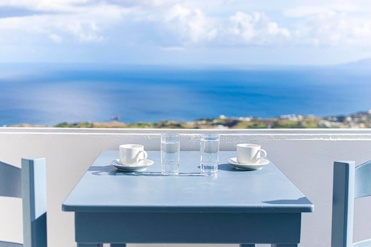 Ein Tisch mit zwei weißen Tassen und zwei Gläsern Wasser, mit Blick auf die Küste.