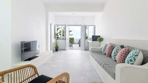 A modern living room with a sofa, a television, and a wicker chair. - Phaos Santorini Suites (Santorini)