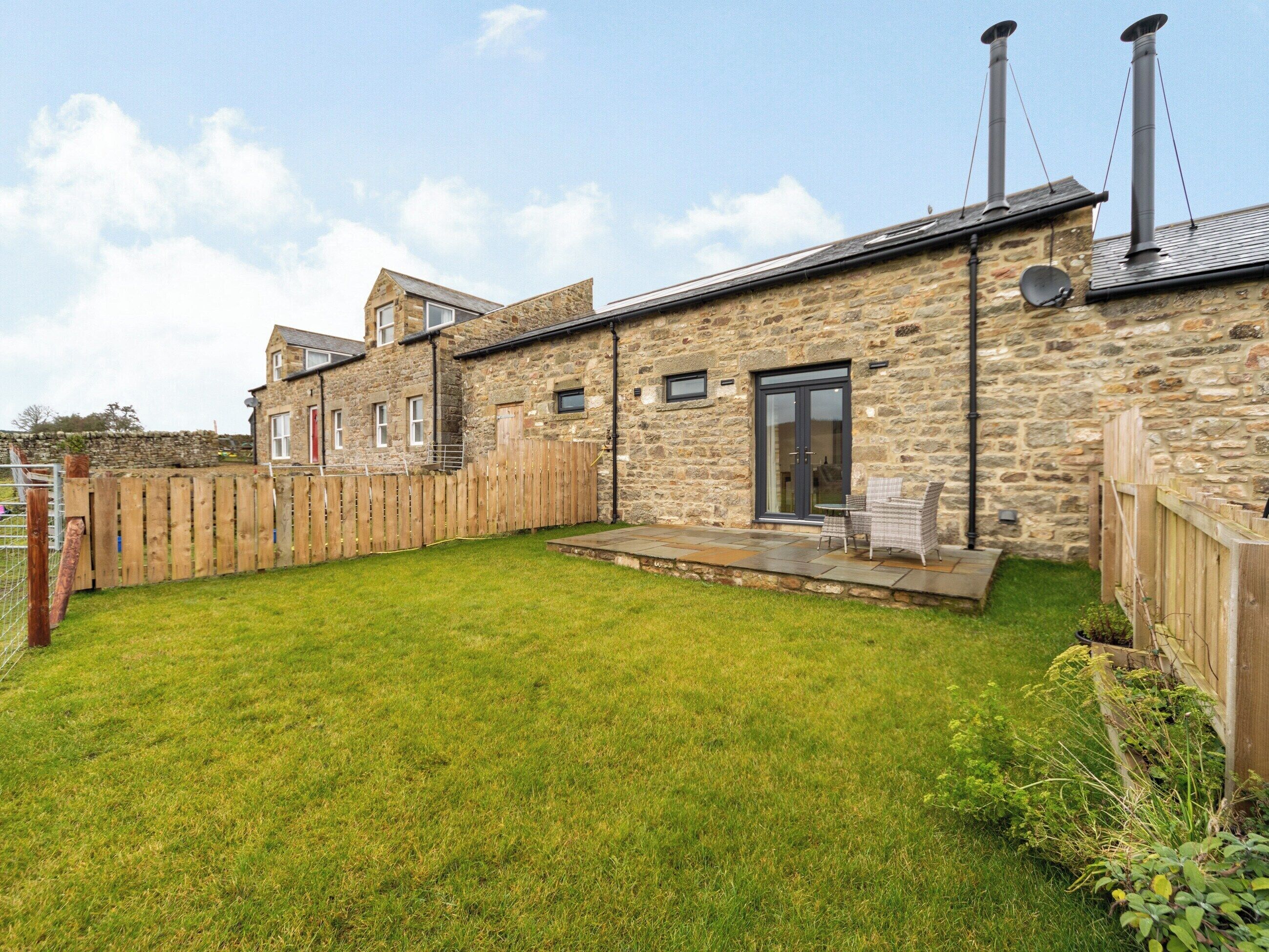 Une maison en pierre avec un jardin clôturé, une terrasse dotée de mobilier d’extérieur et une cheminée.