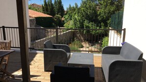 A wooden deck with wicker furniture, a stone wall, and a view of a garden and trees. - Apart 1 (Sleeps 4/6) Overlooking Etang De Thau Bouzigues, Languedoc-Roussillon (Bouzigues)